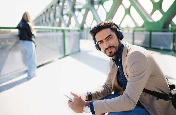 Portrait of young business man commuter with bicycle going to work outdoors in city, using smartphone.