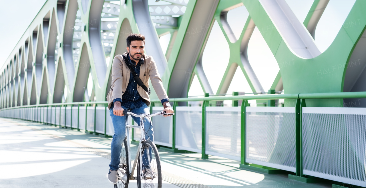 A young business man commuter with bicycle going to work outdoors in city, riding on bridge.