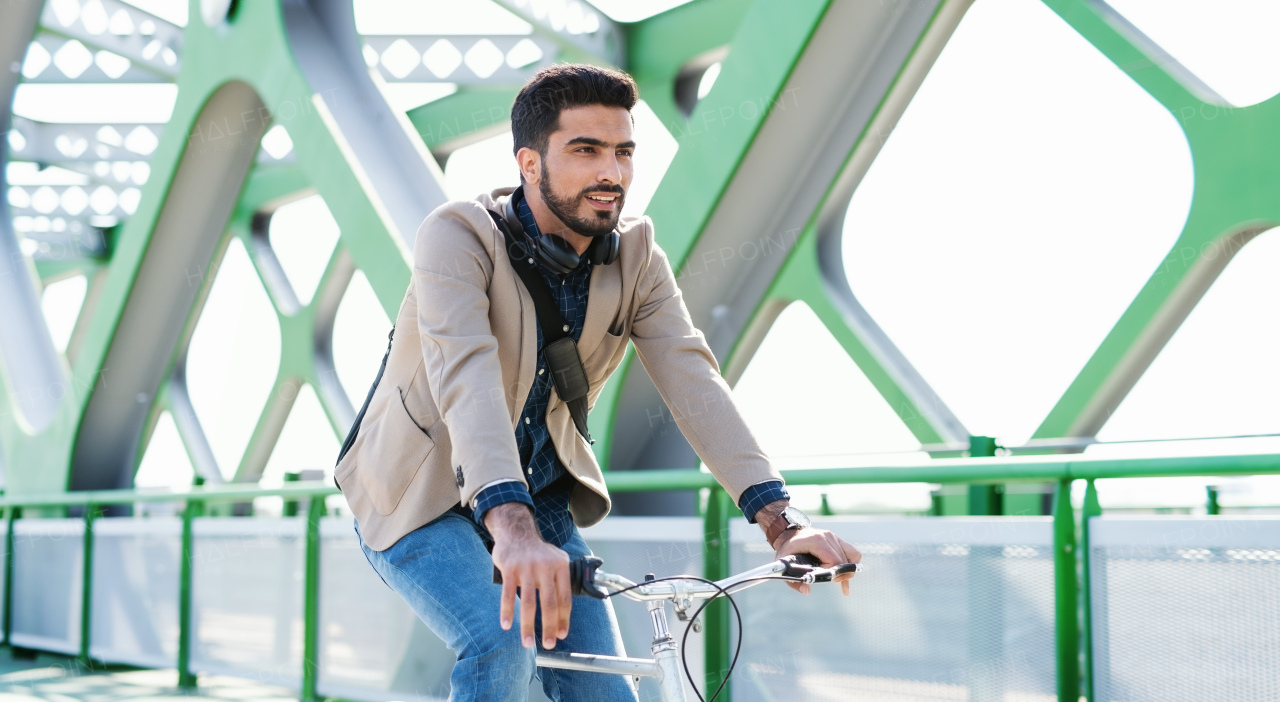 A young business man commuter with bicycle going to work outdoors in city, riding on bridge.