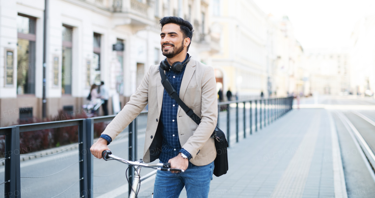 Portrait of young business man commuter with bicycle going to work outdoors in city.