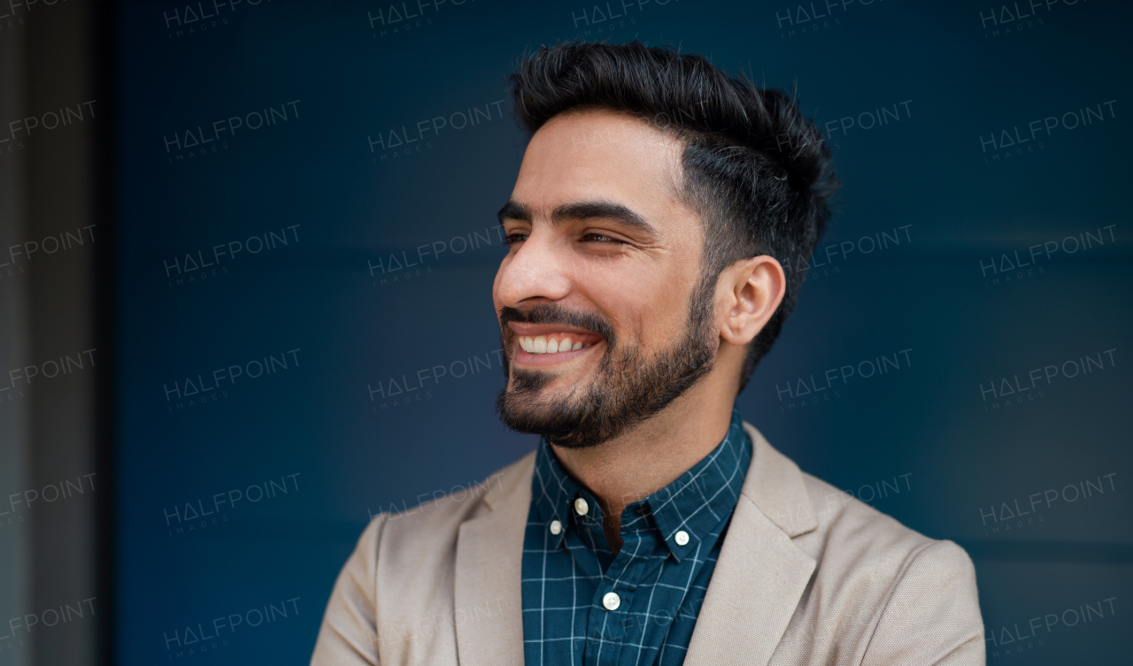 A portrait of young businessman commuter outdoors in city, standing against dark background.