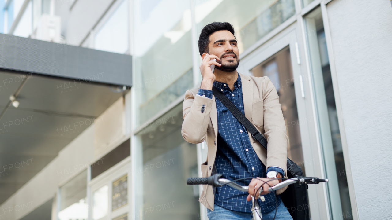 Portrait of young business man commuter with bicycle with smartphonegoing to work outdoors in city.