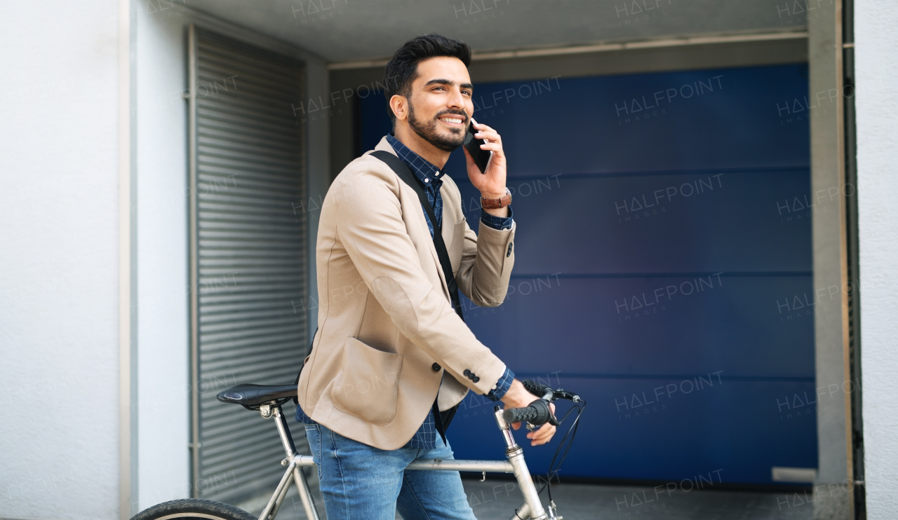 Portrait of young business man commuter with bicycle with smartphonegoing to work outdoors in city.