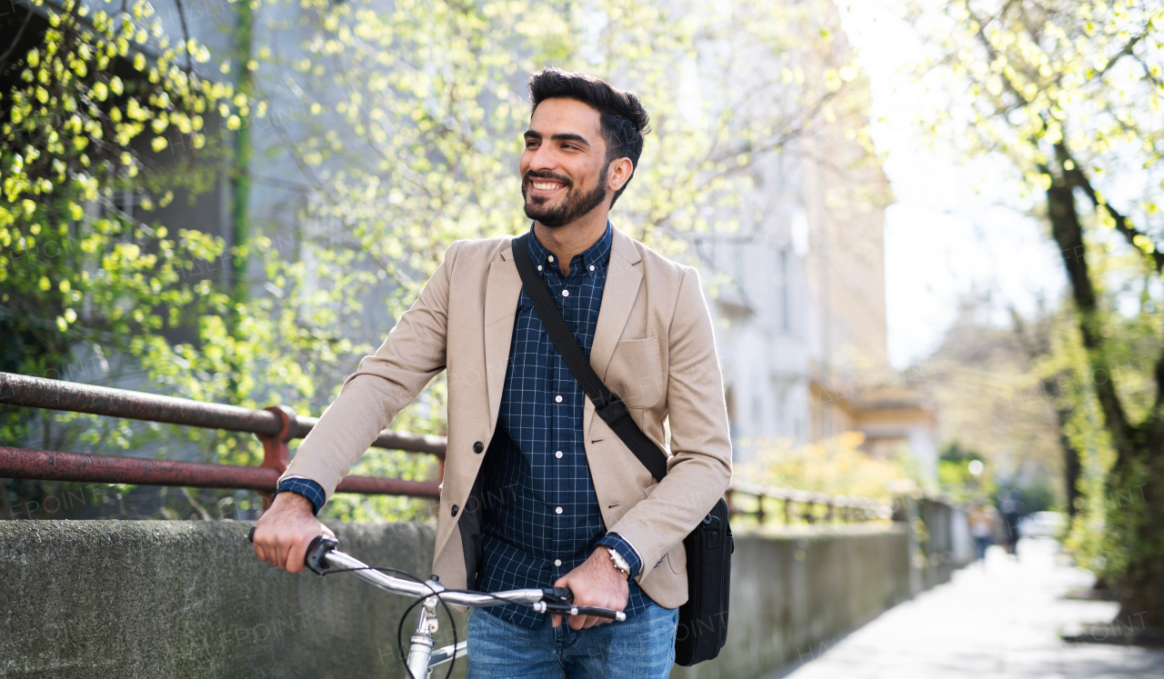 Portrait of young business man commuter with bicycle going to work outdoors in city.