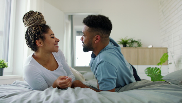 A multiracial young couple in love lying on bed and cuddling together indoors at home.