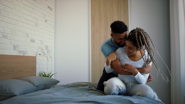 A happy multiracial young couple in love laughing and having fun on bed indoors at home.