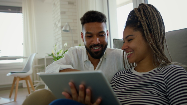 A happy multiracial young couple sitting on floor and using tablet indoors at home.