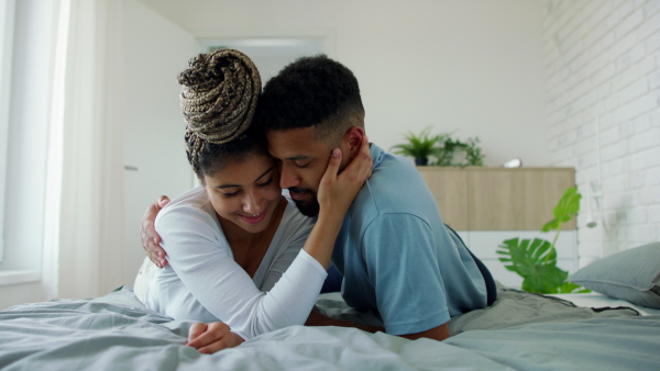 A multiracial young couple in love lying on bed and cuddling together indoors at home.