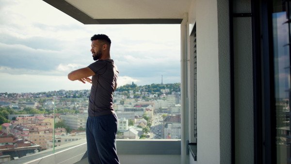 A young sport man doing stretching exercise on balcony outdoors in city.