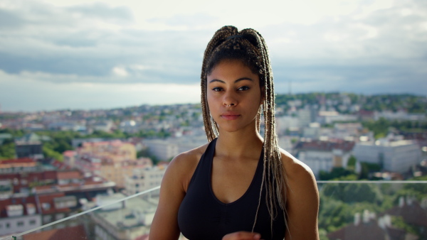 A young sport woman standing with arms crossed and looking at camera on balcony outdoors in city.