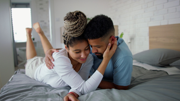 A multiracial young couple in love lying on bed and cuddling together indoors at home.