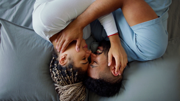 A top view of multiracial young couple in love lying on bed and cuddling together indoors at home.