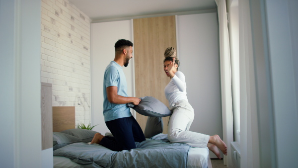 A happy multiracial young couple in love having fun on bed indoors at home, pillow fight.