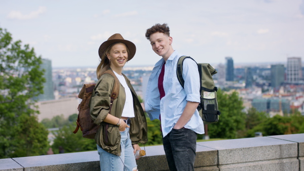 A young couple travelers in city on holiday, looking at camera. Cityscape in the background.