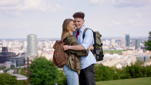 Happy young couple travelers in city on holiday, hugging and looking at camera. Cityscape in the background.