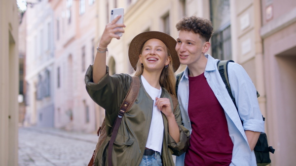 A young couple travelers with smartphone sightseeing in city on holiday, taking selfie.