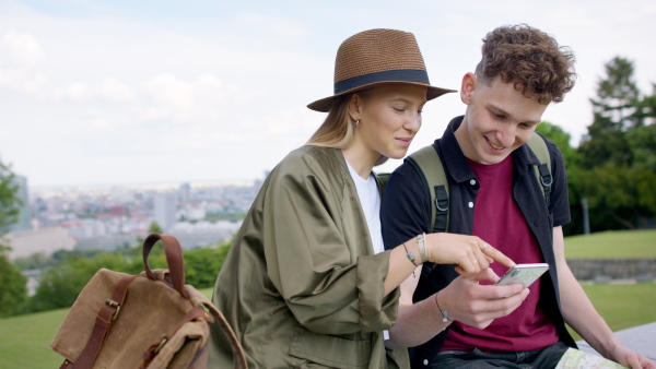 A young couple travelers with map in city on holiday, using smartphone.