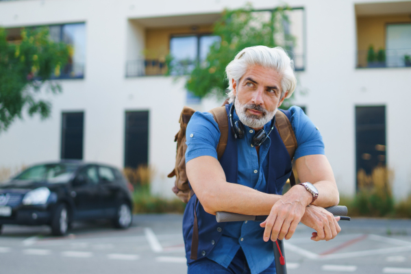 Portrait of mature man commuter with electric scooter outdoors in city, resting.