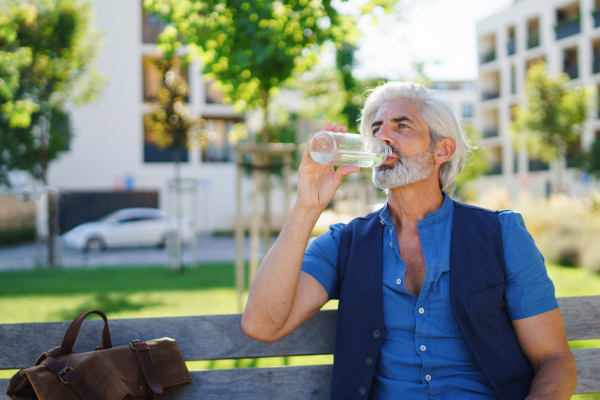 Portrait of mature man sitting outdoors in city, drinking water. Copy space.