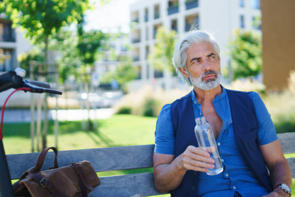 Portrait of handsome mature man sitting outdoors in city, holding water bottle.