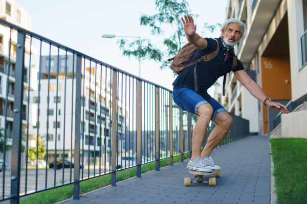 Front view portrait of mature man riding skateboard outdoors in city, going back to work.