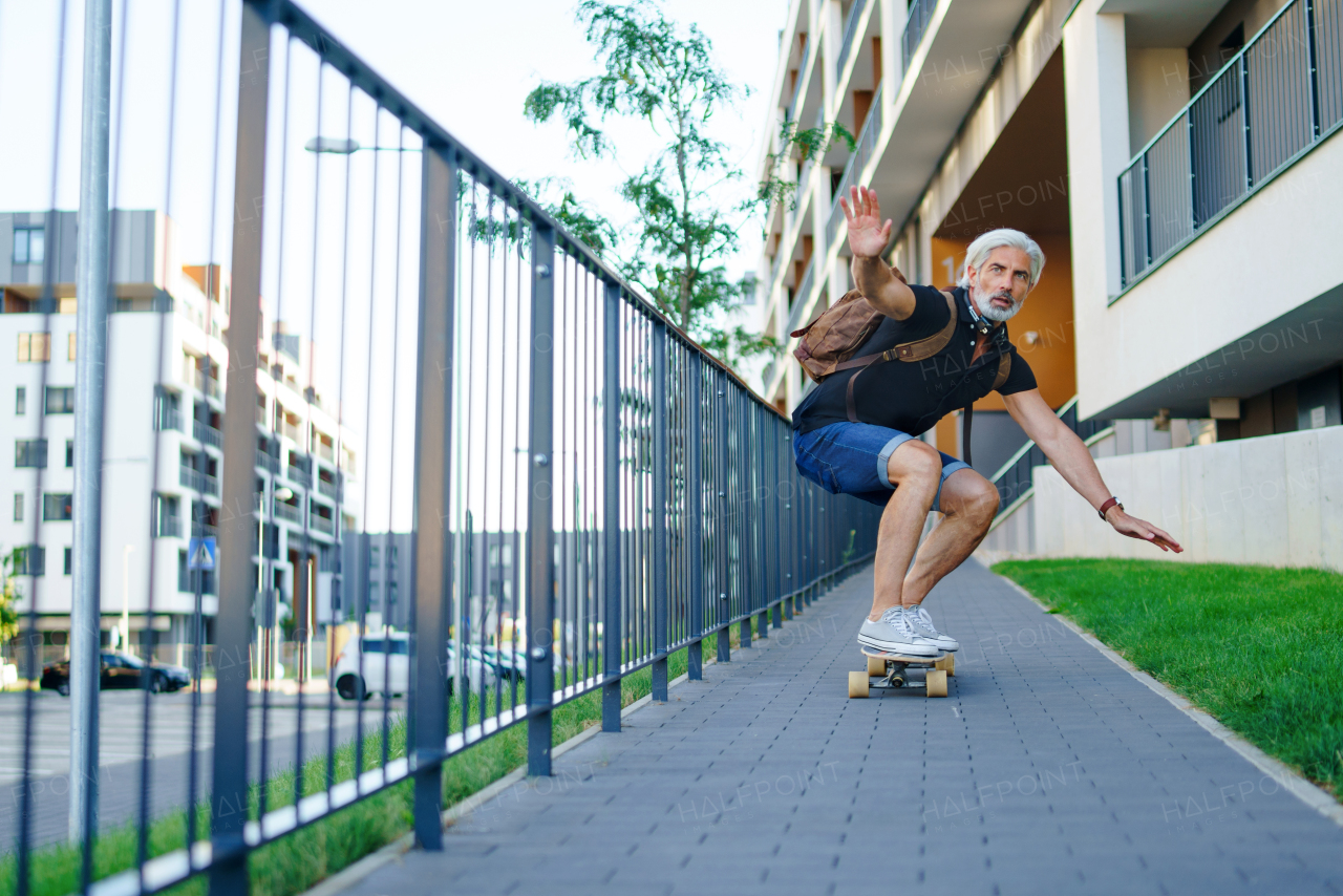 Front view portrait of mature man riding skateboard outdoors in city, going back to work.