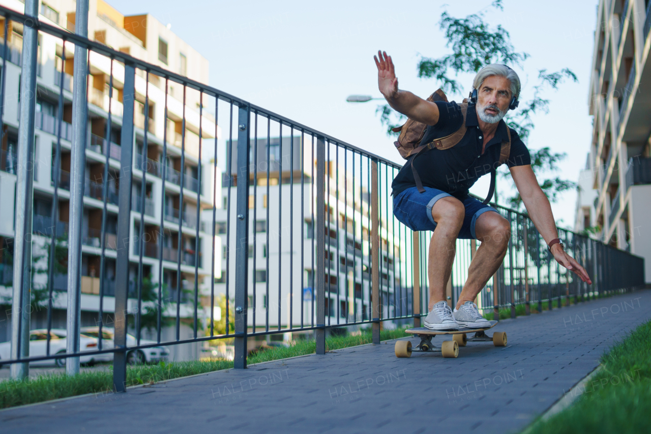 Front view portrait of mature man riding skateboard outdoors in city, going back to work.