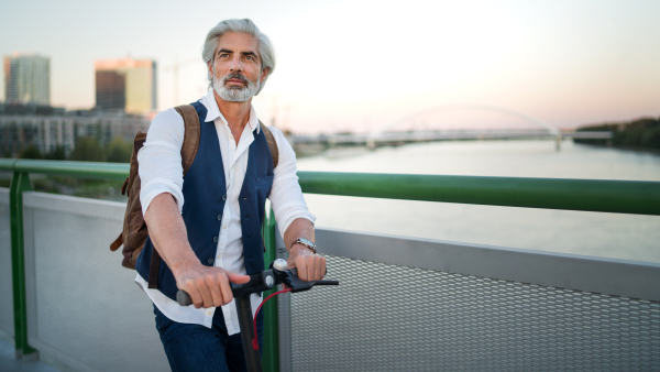 Portrait of mature man commuter with electric scooter outdoors in city, going to work. Copy space.