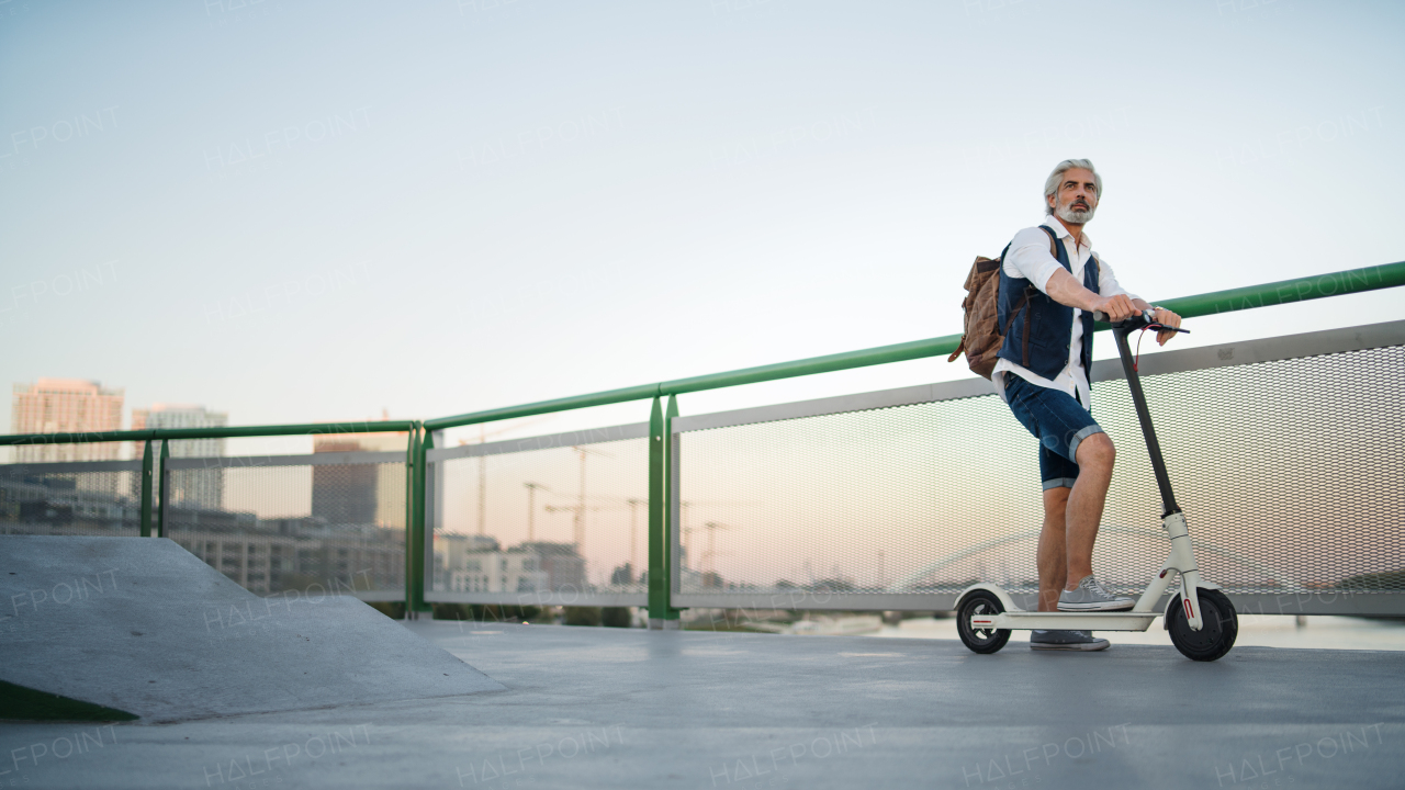 Mature man commuter with electric scooter outdoors in city, going to work. Copy space.