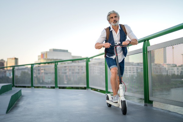 Mature man commuter with electric scooter outdoors in city, going to work. Copy space.