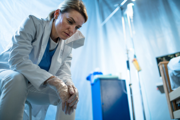 Tired and frustrated doctor sitting by empty bed in hospital, coronavirus concept.