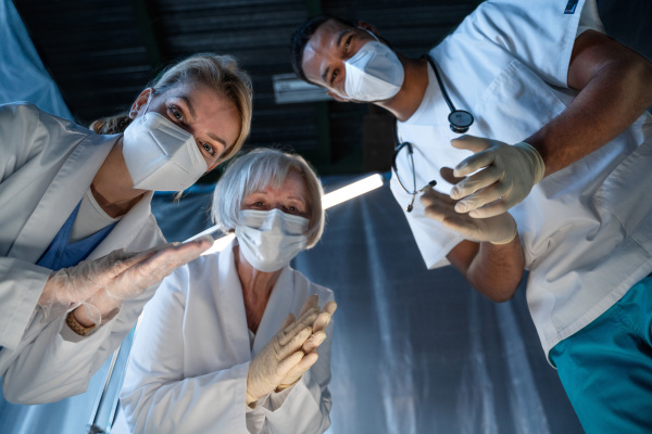 Bottom view of cheerful doctors leaning over covid-19 patient n hospital, clapping. Coronavirus and recovery concept.