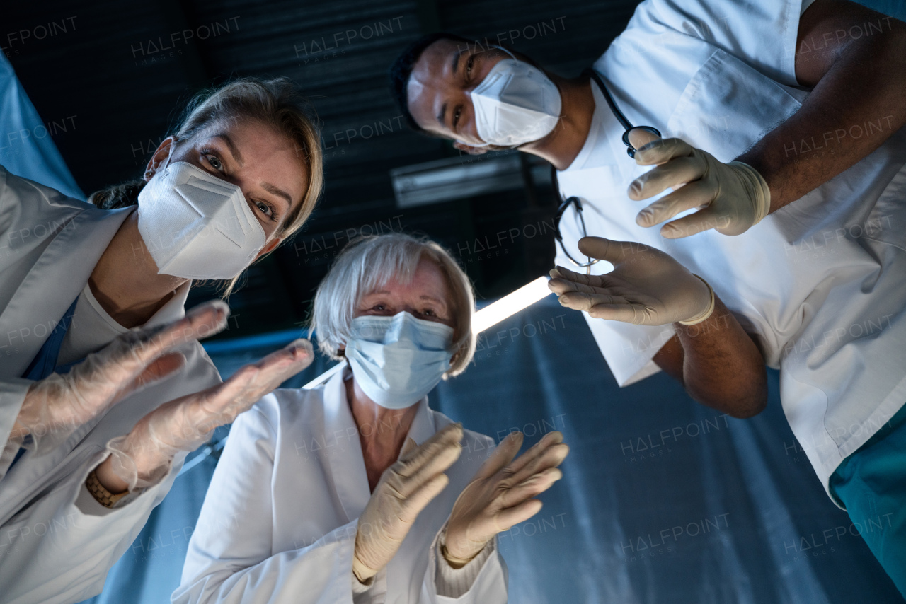 Bottom view of cheerful doctors leaning over covid-19 patient n hospital, clapping. Coronavirus and recovery concept.