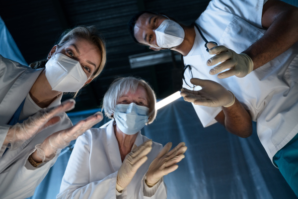 Bottom view of cheerful doctors leaning over covid-19 patient n hospital, clapping. Coronavirus and recovery concept.