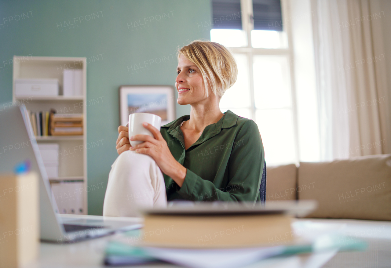 Portrait of happy business woman indoors in office sitting at desk, holding cup of tea.