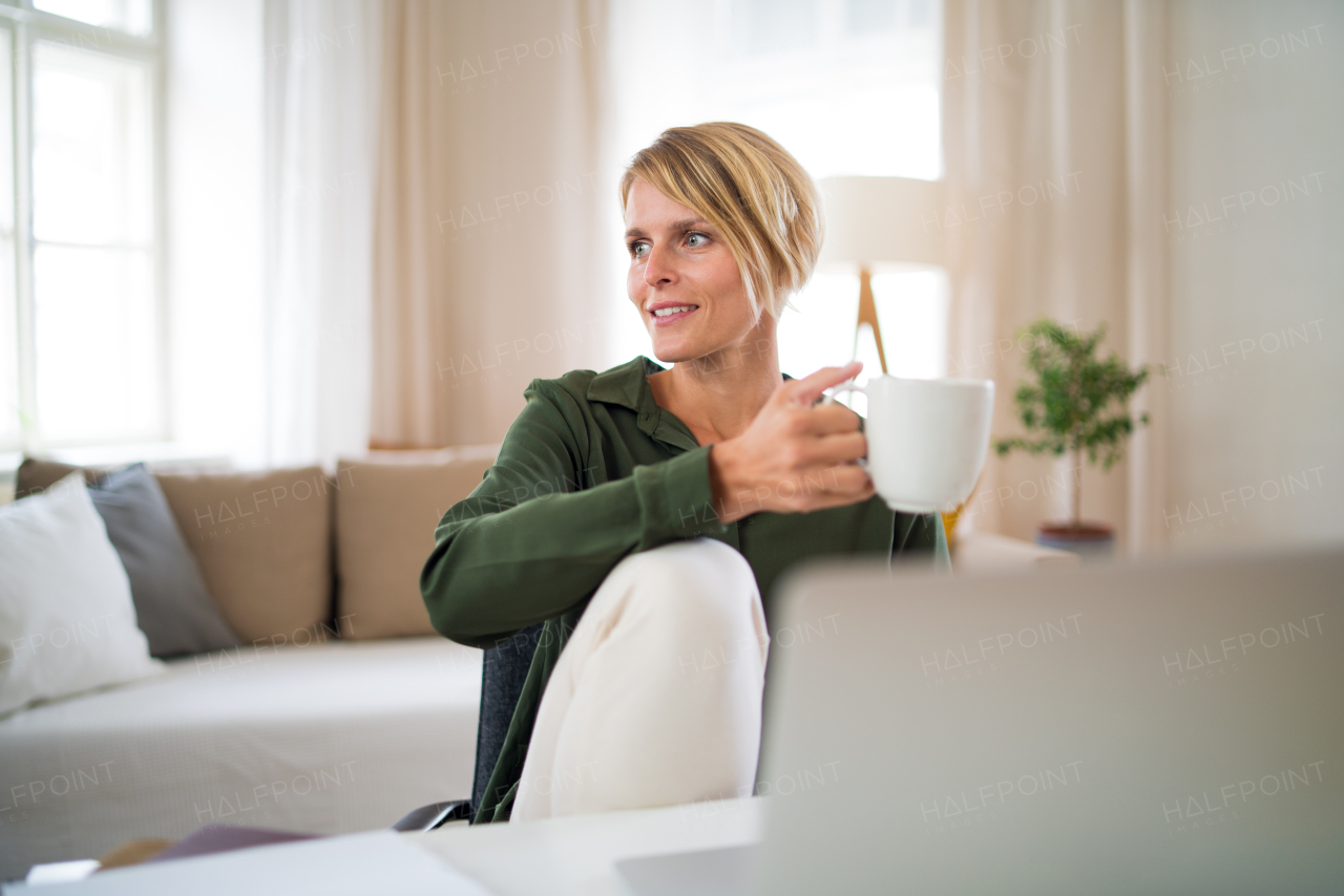 Portrait of happy business woman indoors in office sitting at desk, holding cup of tea.