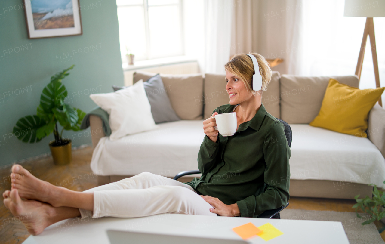 Portrait of happy business woman indoors in office sitting at desk, holding cup of tea.