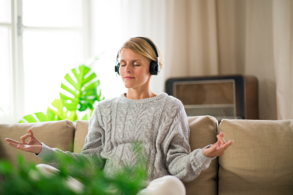 Portrait of woman indoors at home doing yoga, on sofa, mental health and meditation concept.