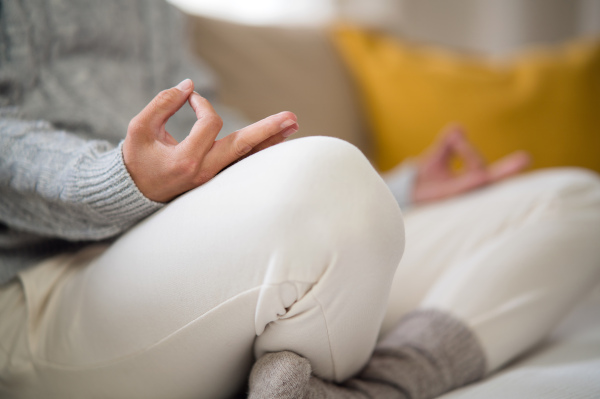 Midsection of unrecognizable woman indoors at home doing yoga, on sofa, mental health and meditation concept.