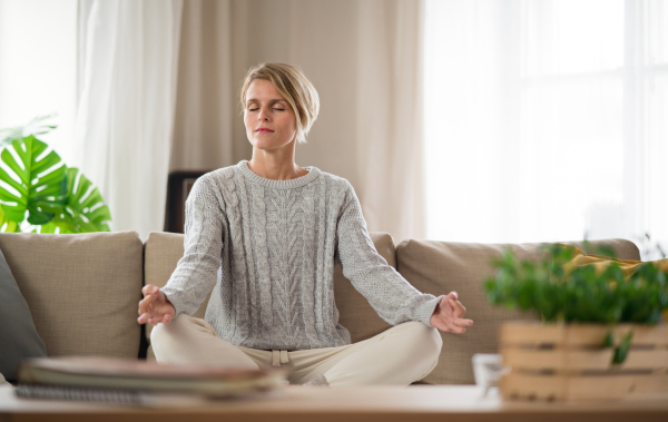 Portrait of woman indoors at home doing yoga, on sofa, mental health and meditation concept.