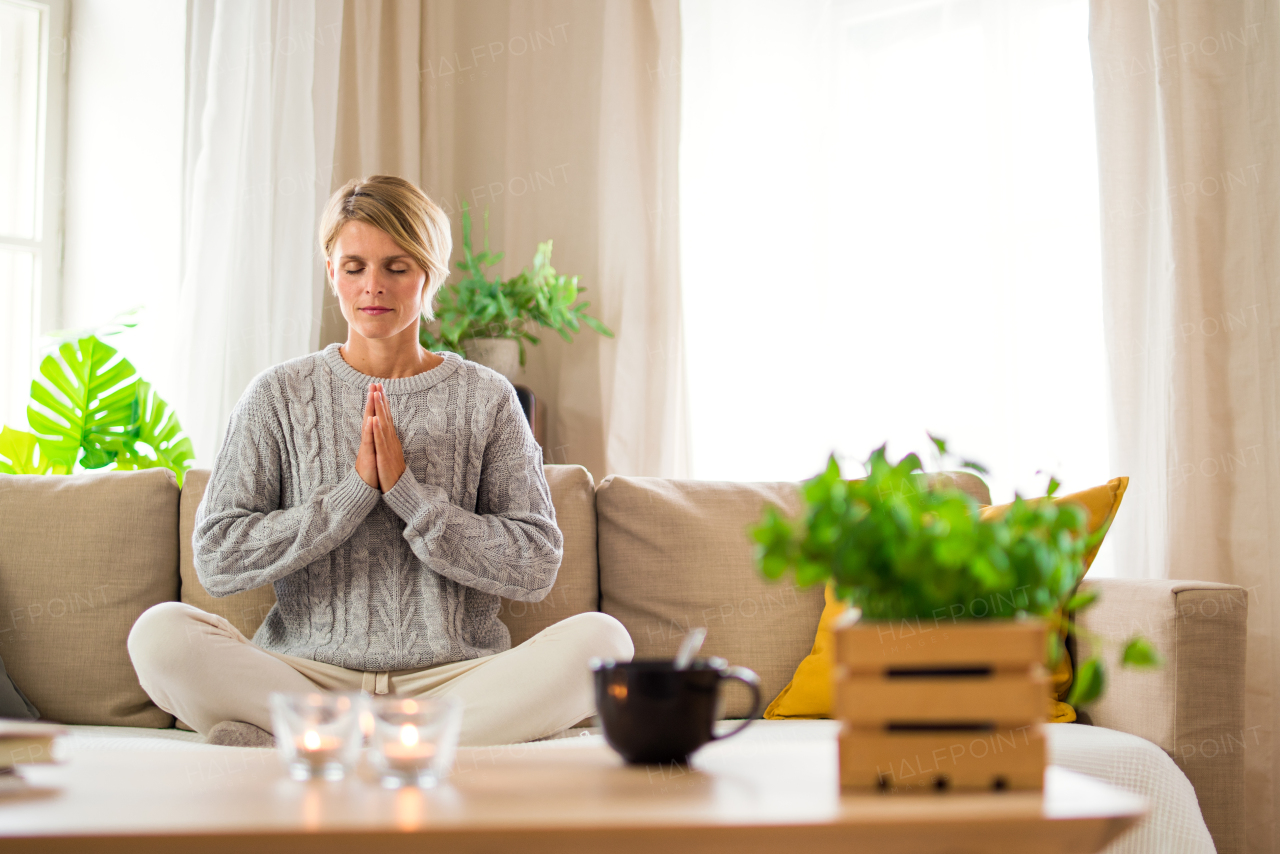 Portrait of woman indoors at home doing yoga, on sofa, mental health and meditation concept.