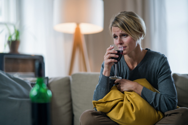 Depressed and lonely woman with wine indoors at home, mental health and alcohol addiction concept.