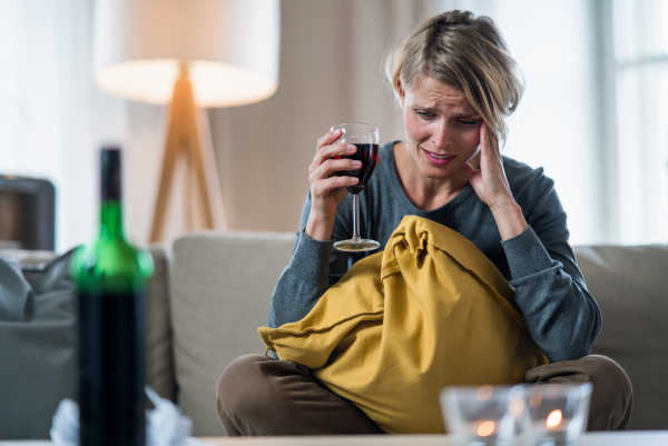 Depressed woman with wine indoors at home, mental health and alcohol addiction concept.