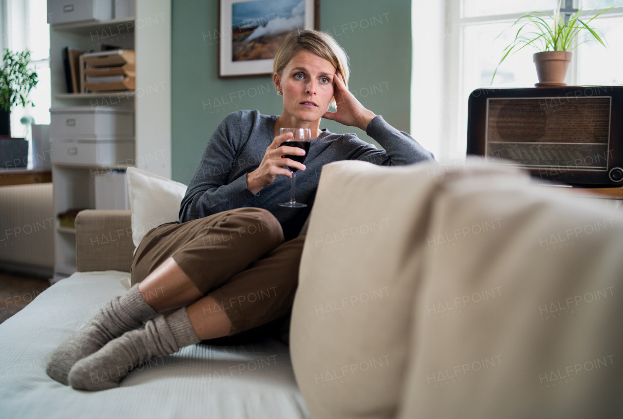 Depressed and lonely woman with wine indoors at home, mental health and alcohol addiction concept.