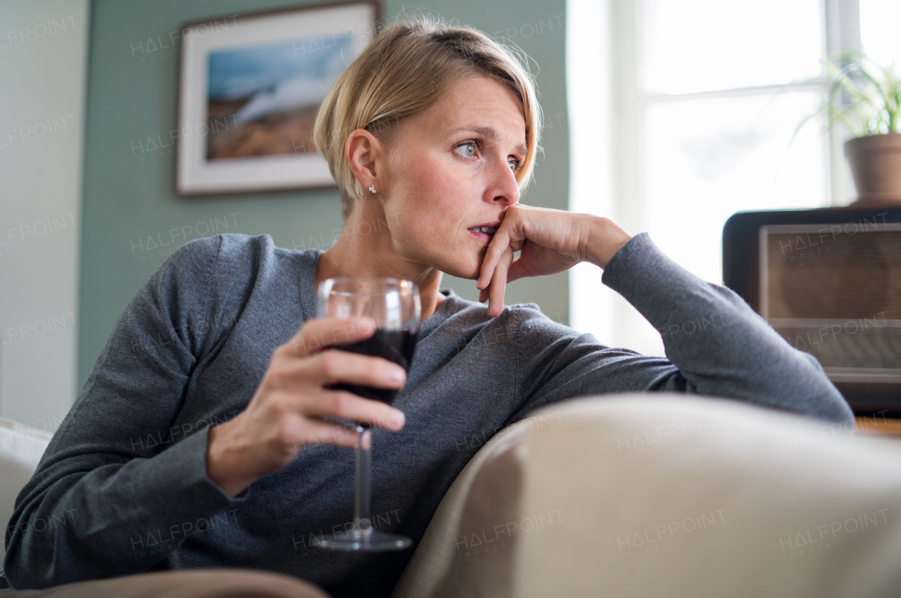 Depressed and lonely woman with wine indoors at home, mental health and alcohol addiction concept.