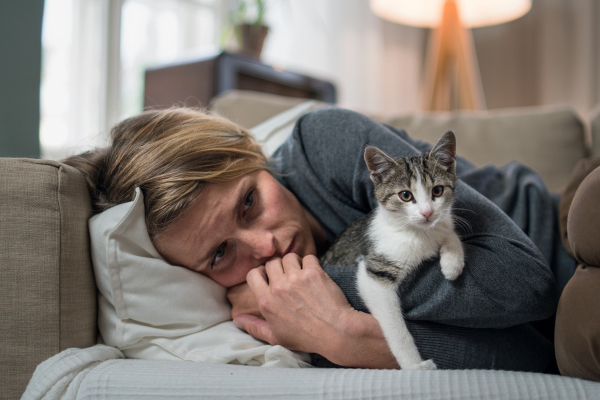 Woman with cat indoors on sofa at home feeling stressed, mental health concept.