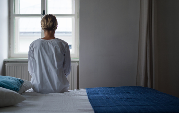 Rear view of woman patient sitting on bed in hospital feeling stressed, mental health and coronavirus concept. Copy space.