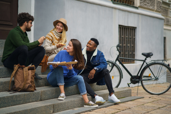 Group of cheerful young people outdoors in town, eating pizza. Coronavirus concept.