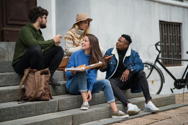 Group of cheerful young people outdoors in town, eating pizza. Coronavirus concept.