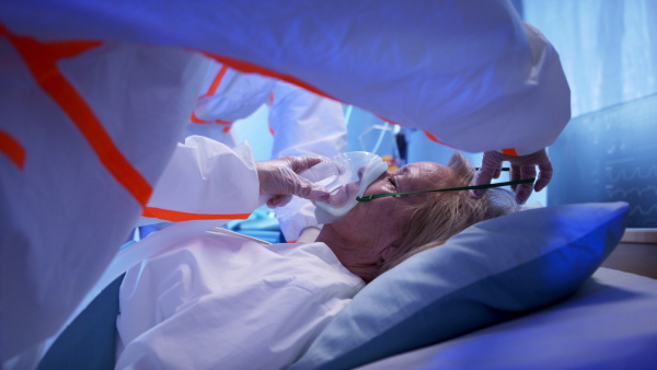 Side view of doctors and covid-19 infected patient with oxygen mask in bed in hospital, coronavirus concept